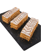 Drei frisch zubereitete Mille-feuilles auf einer schwarzen Schieferplatte. Zu sehen sind goldbraune Blätterteigschichten, eine weiße Cremefüllung und die charakteristische braune Zickzack-Verzierung auf der glatten Zuckerglasur.