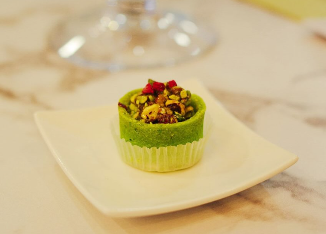 Eine Spezialität von La Maison des Délices; ein luxuriöses Dessert im grünen Pistazienmantel, verziert mit Granatapfelkernen und Pistazienstückchen.