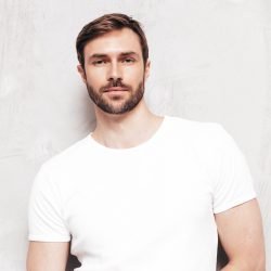 Portrait of handsome smiling stylish hipster lambersexual model. Sexy man dressed in T-shirt and jeans. Fashion male isolated on blue wall in studio